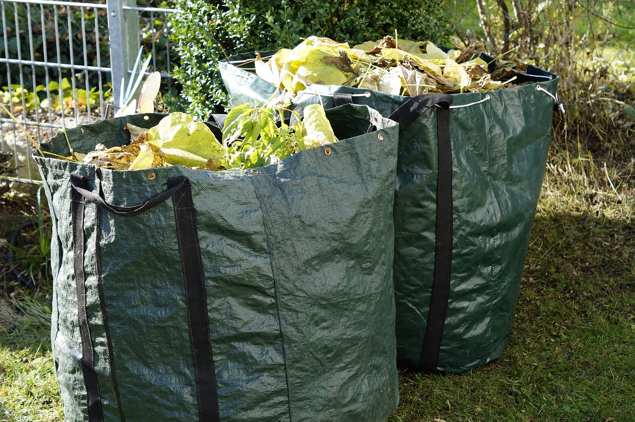deux grands sacs de déchets verts remplis de feuilles et de tailles de haie dans un jardin