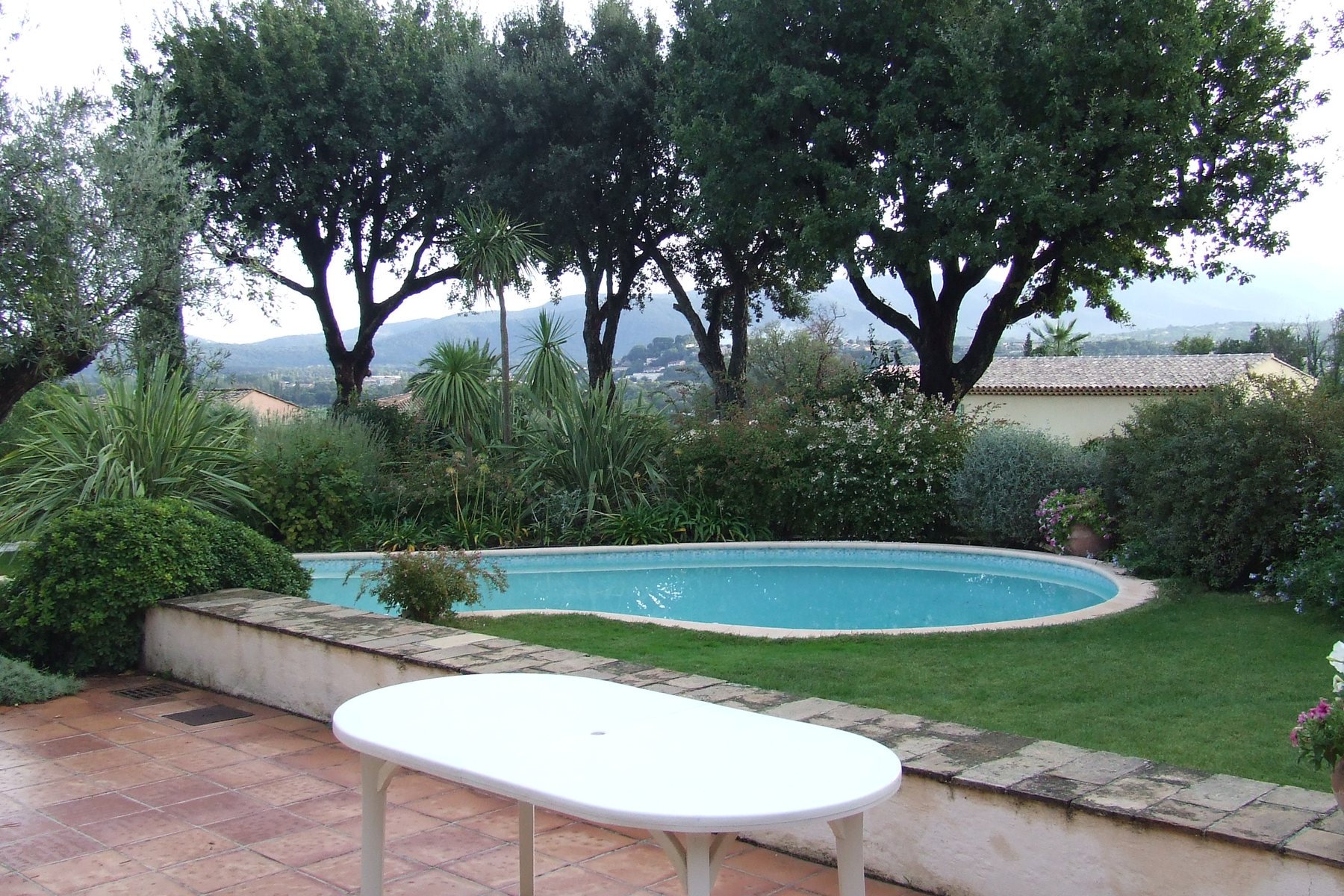 jardin méditerranéen en France avec une piscine de forme libre, une pelouse et une terrasse carrelée au premier plan